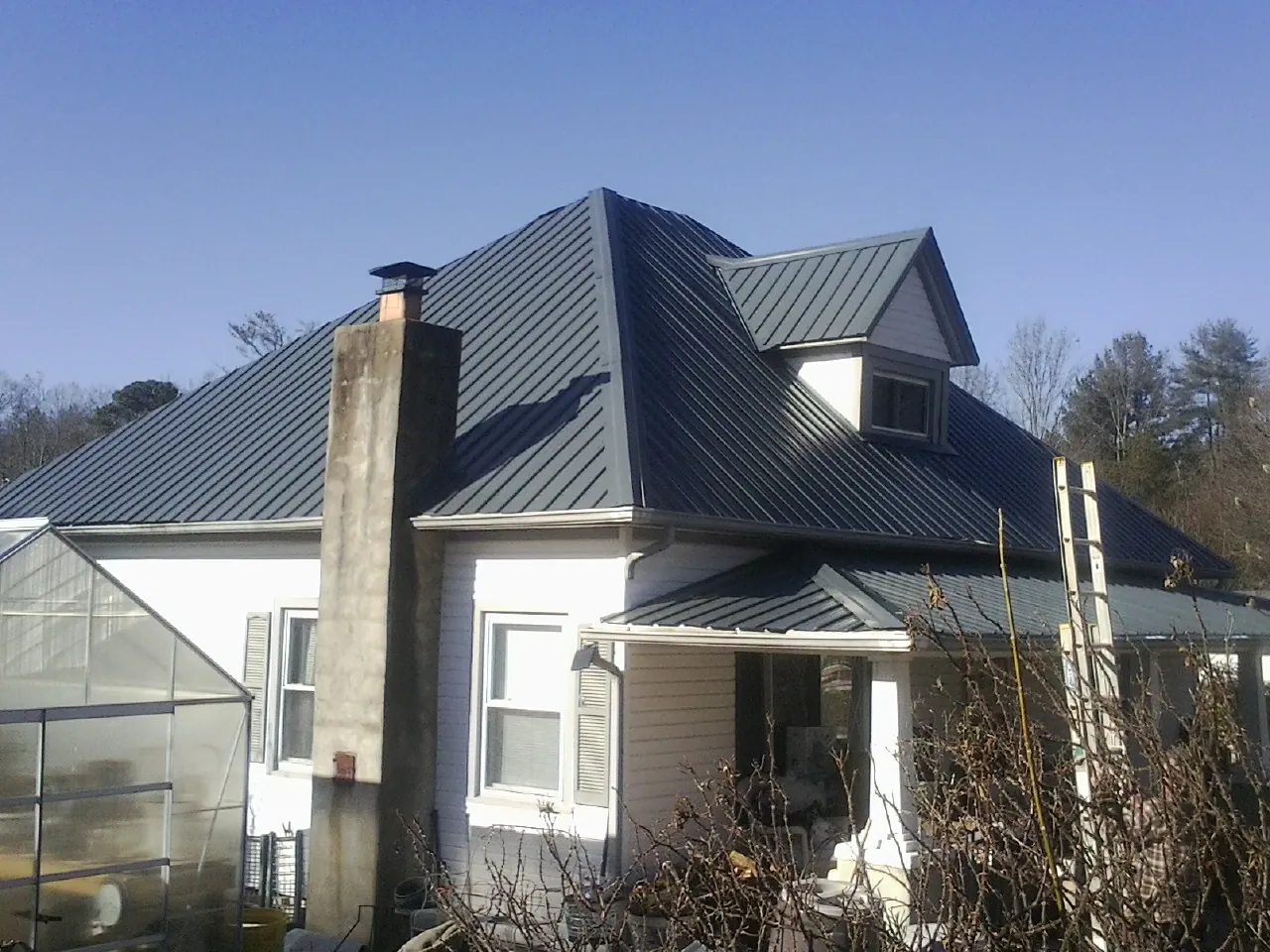 Dark blue standing seam metal roof on a white farmhouse with dormer — Slate & Tile Roof Repair by Roofing Brothers in Still Pond