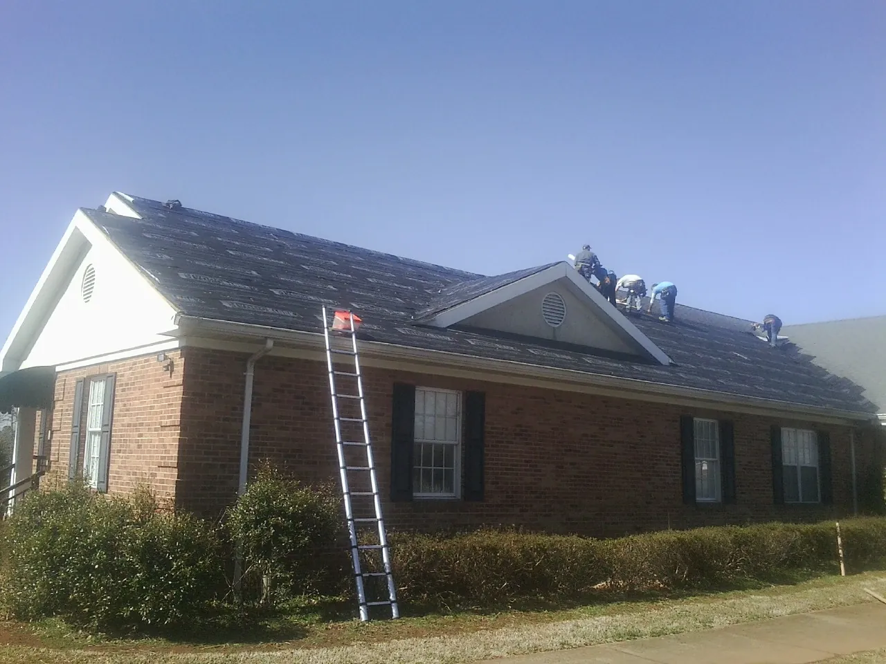 Crew tearing shingles off a brick ranch roof with a ladder set — Emergency Roof Repair work by our crew in Still Pond