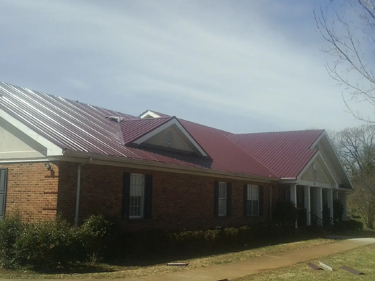 Red metal roof with gabled entries on a long brick building, from a Hail Damage Roof Repair job in Still Pond