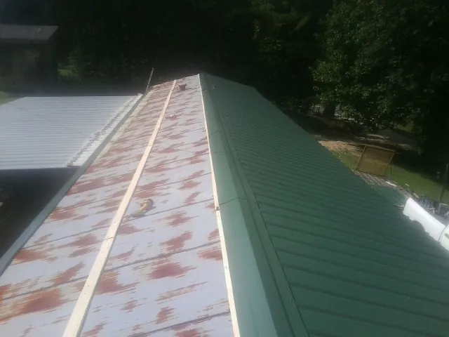 Old rusted panels beside newly installed green metal roofing — Wind Damage Roof Repair by Roofing Brothers in Still Pond