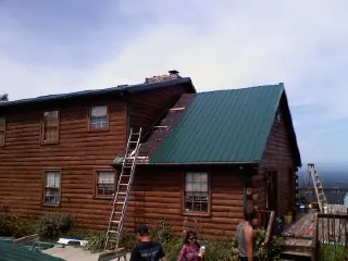 Green metal roof going on a two story log home with ladders set in Still Pond