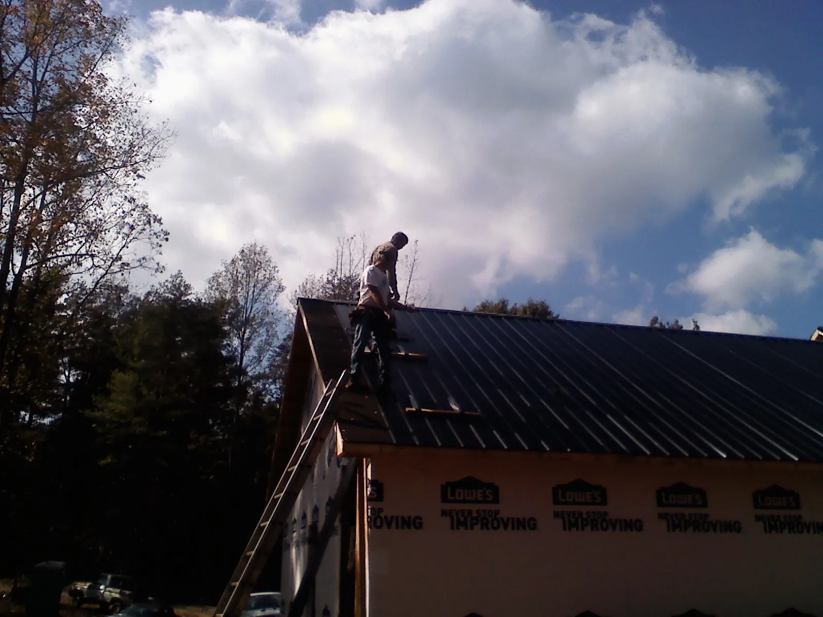 Roofer fastening dark metal panels high against a cloudy sky, from a Roof Inspection job in Still Pond