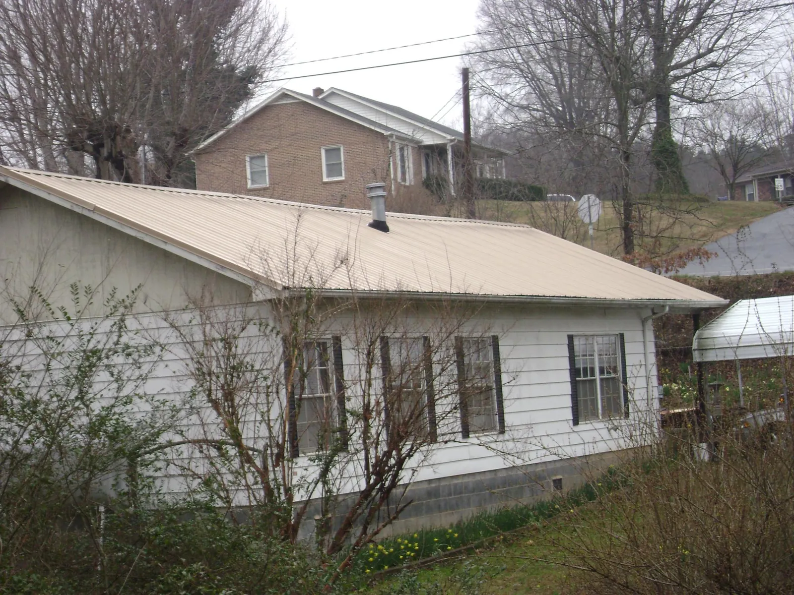 Tan metal roof on a white sided house set into a hillside — Commercial Roofing by Roofing Brothers in Still Pond